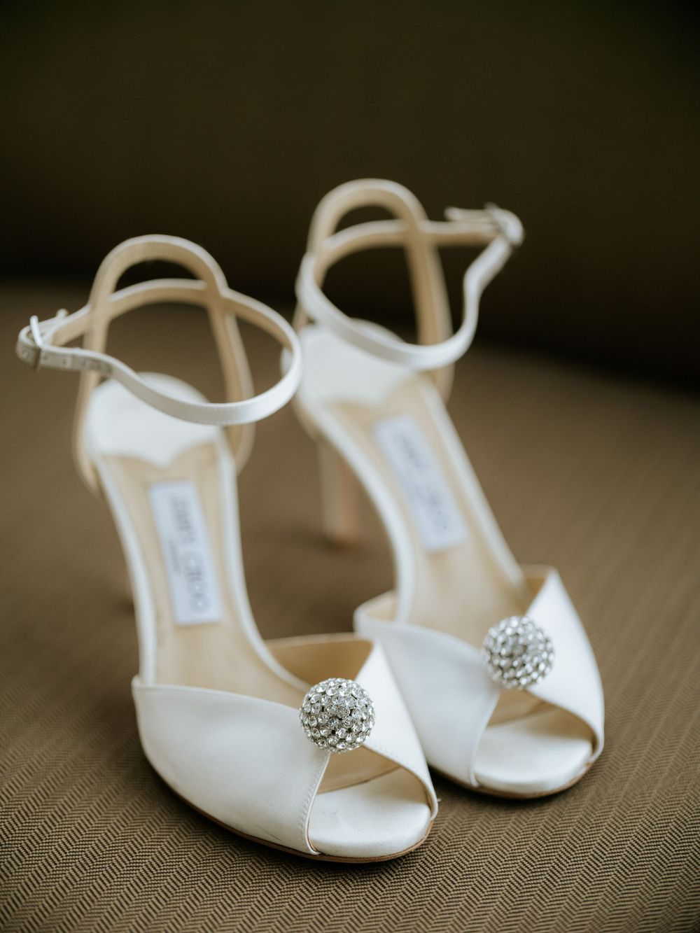 White bridal shoes with crystal embellishments photographed against a neutral textured background.