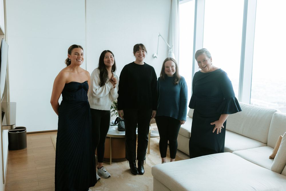 A group wearing black formal attire stands together in a bright white room with natural lighting.