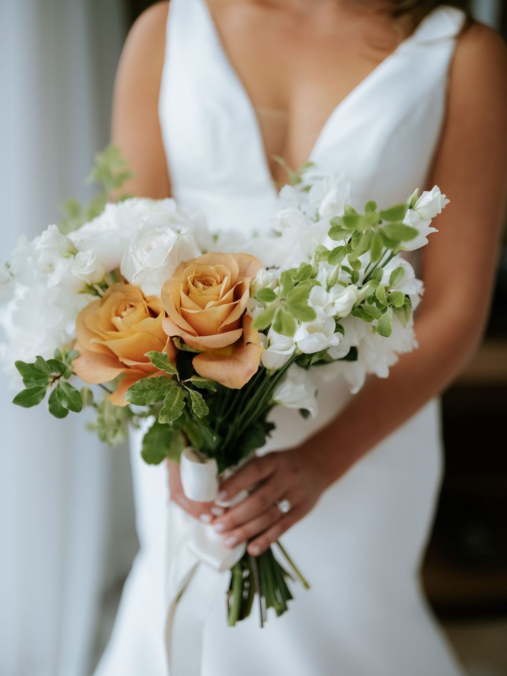 A series of elegant wedding bouquets featuring peach roses and white flowers held against a white dress.