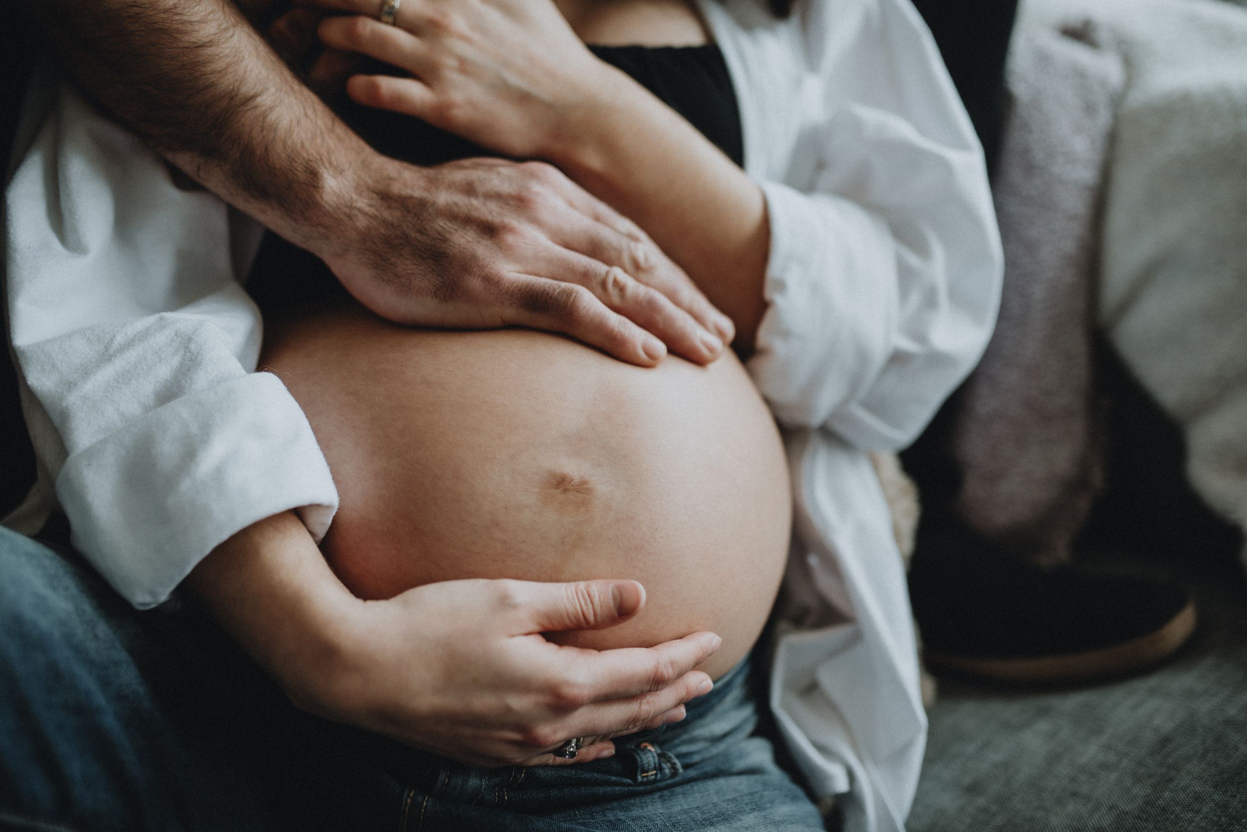 Hands from both parents cradle a pregnant belly during a maternity session in Cochrane Alberta