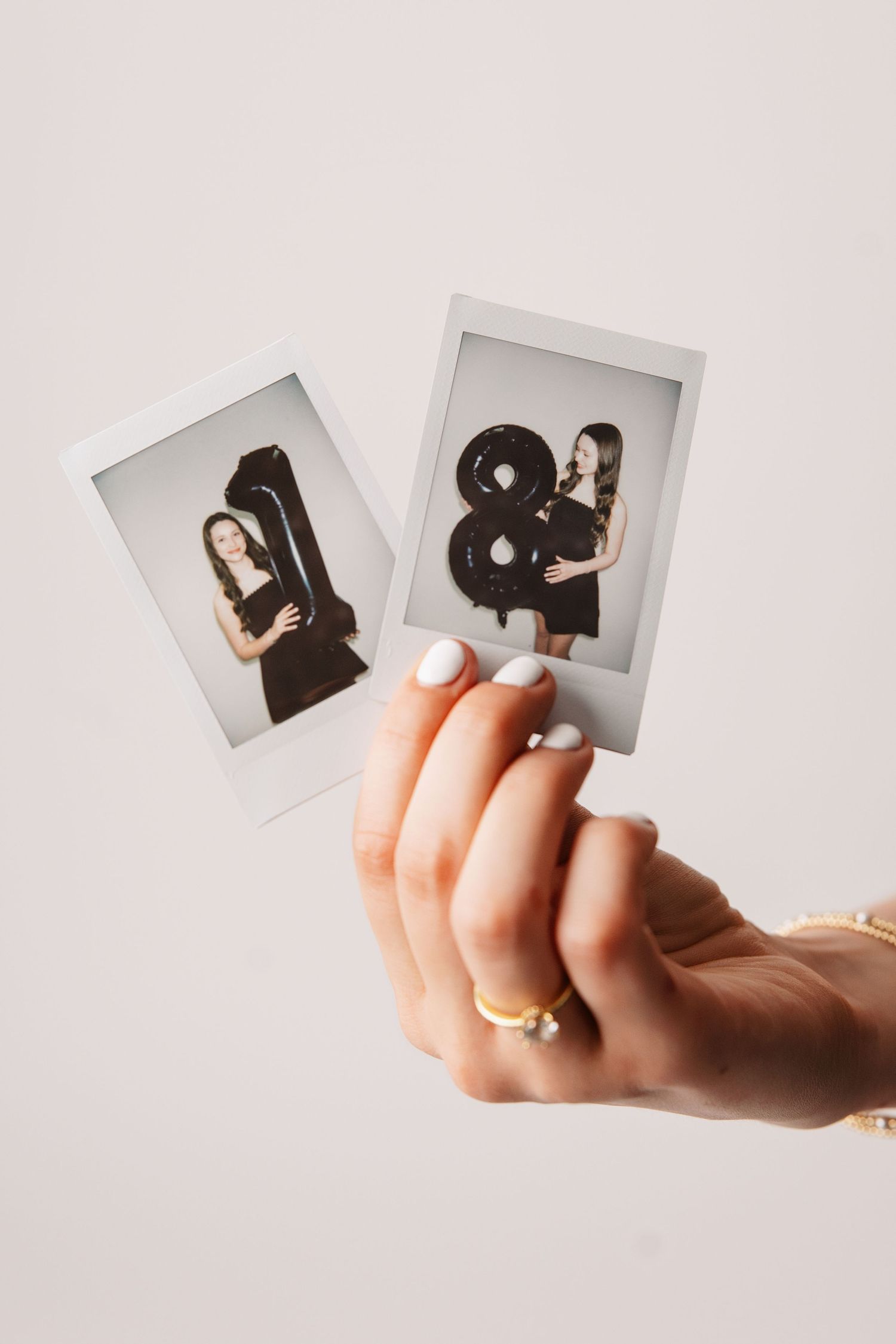 Hand holding two vintage Polaroid photos with numbers 1 and 8 against a light background.