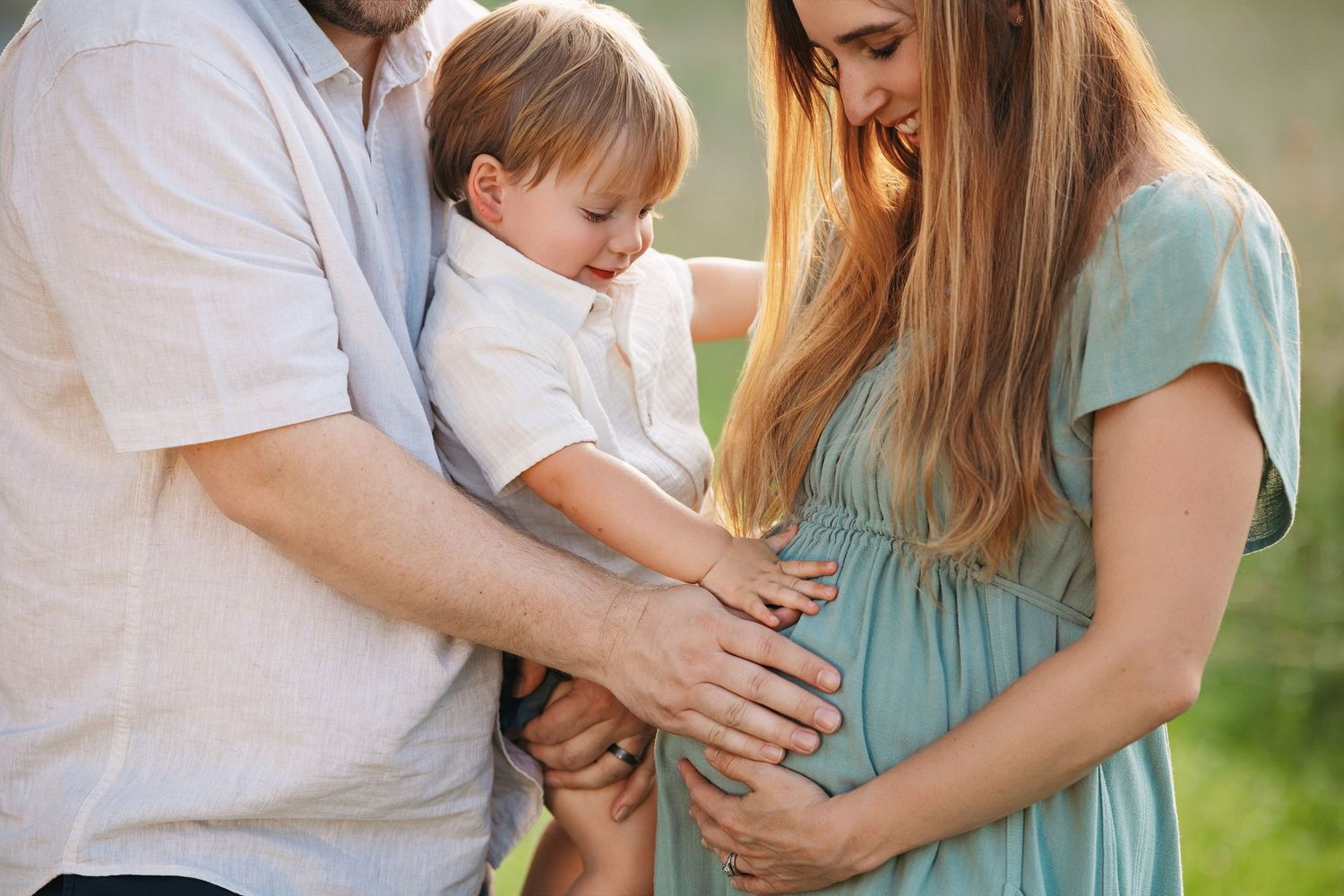 Expectant couple with toddler sibling sharing a moment during a professional maternity photoshoot outdoors.