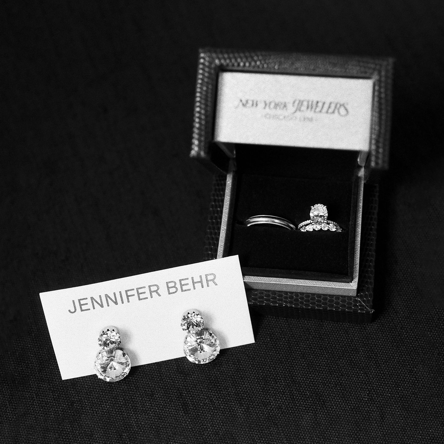 Jennifer Behr crystal drop earrings beside a diamond ring in a New York Jewelers box.