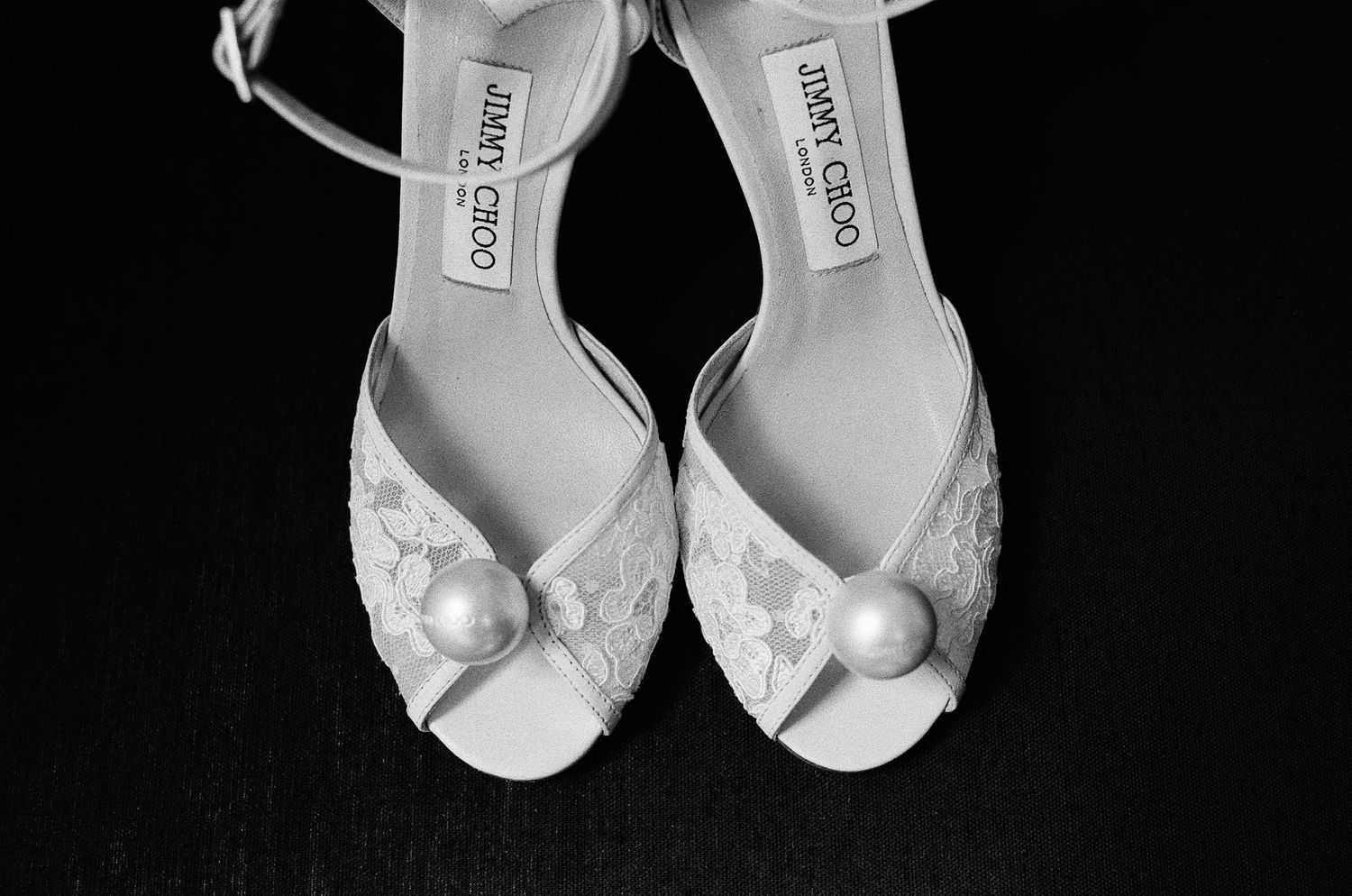 Black and white photo of Jimmy Choo lace bridal heels with pearl embellishments.