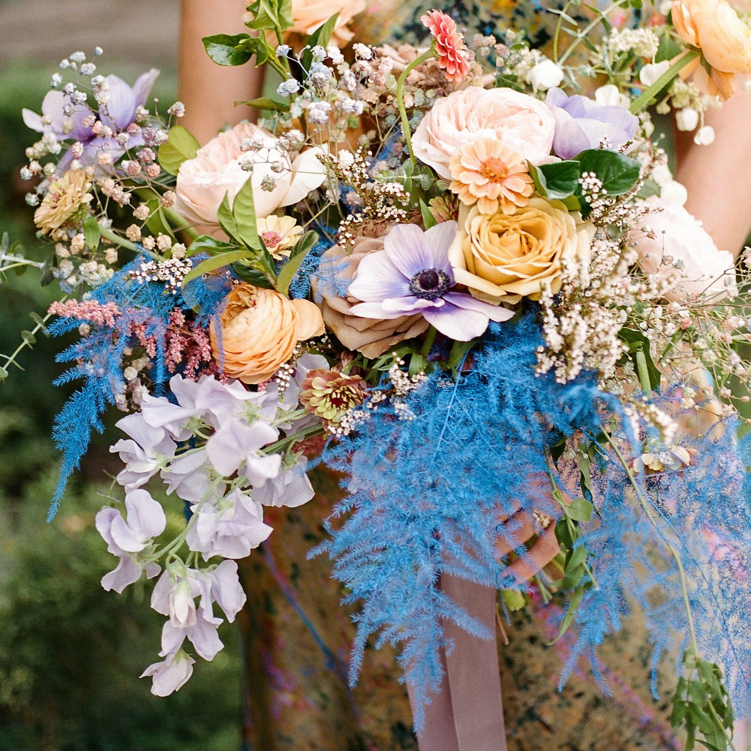 Colorful wedding bouquet with blue, peach, and purple flowers with flowing ribbons.