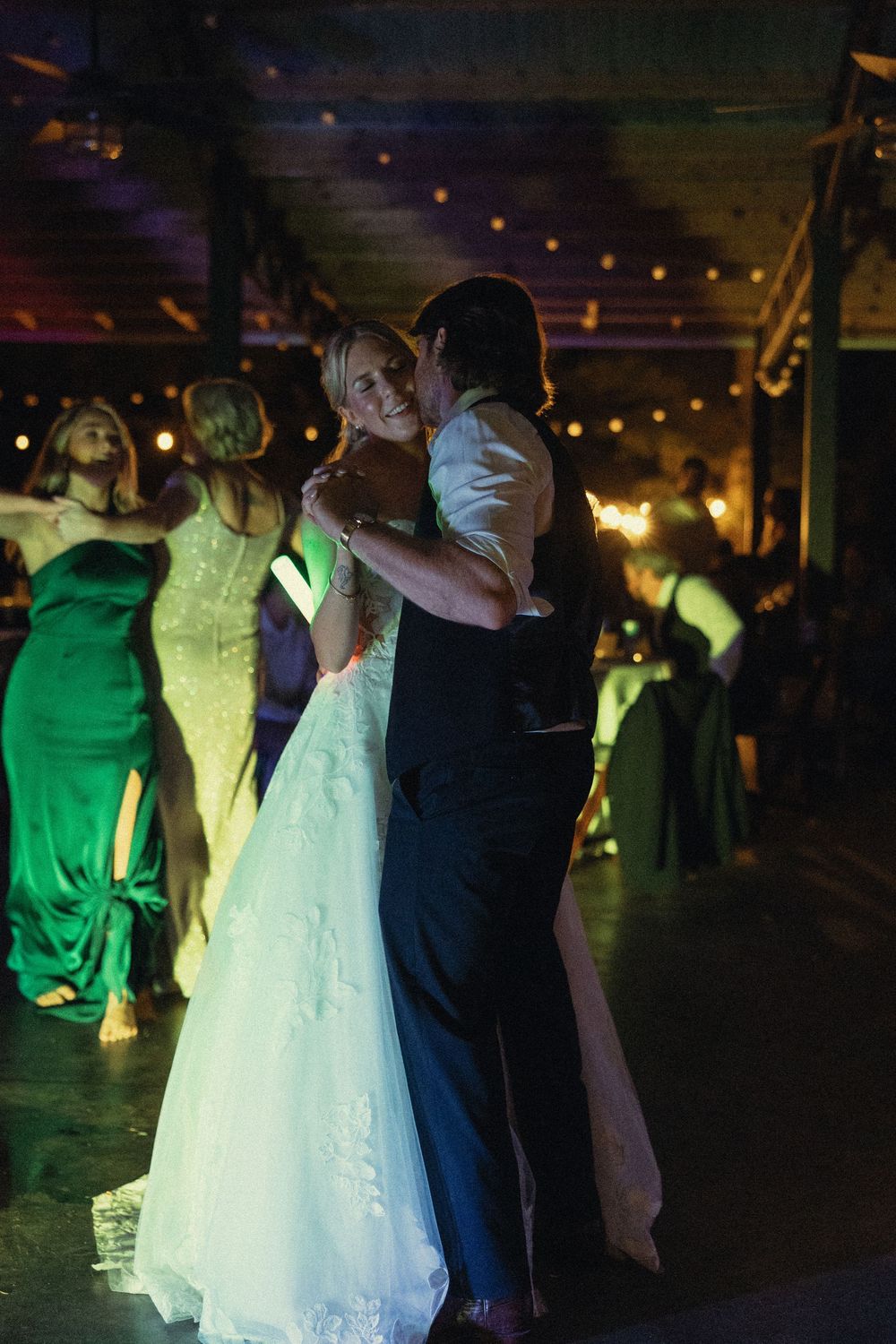 A couple shares their first dance at a wedding reception under romantic string lights with guests watching at The Elms of Coosada in Alabama