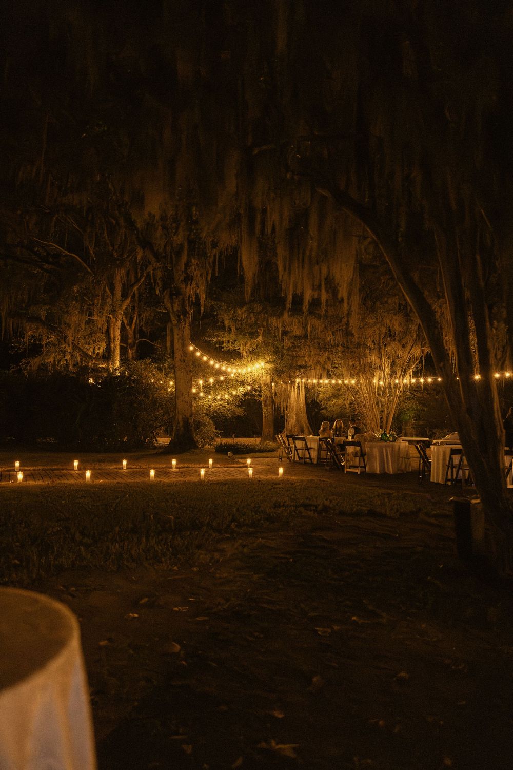 String lights illuminate a dark outdoor gathering space with chairs arranged under a canopy of trees at night in Coosada, Alabama