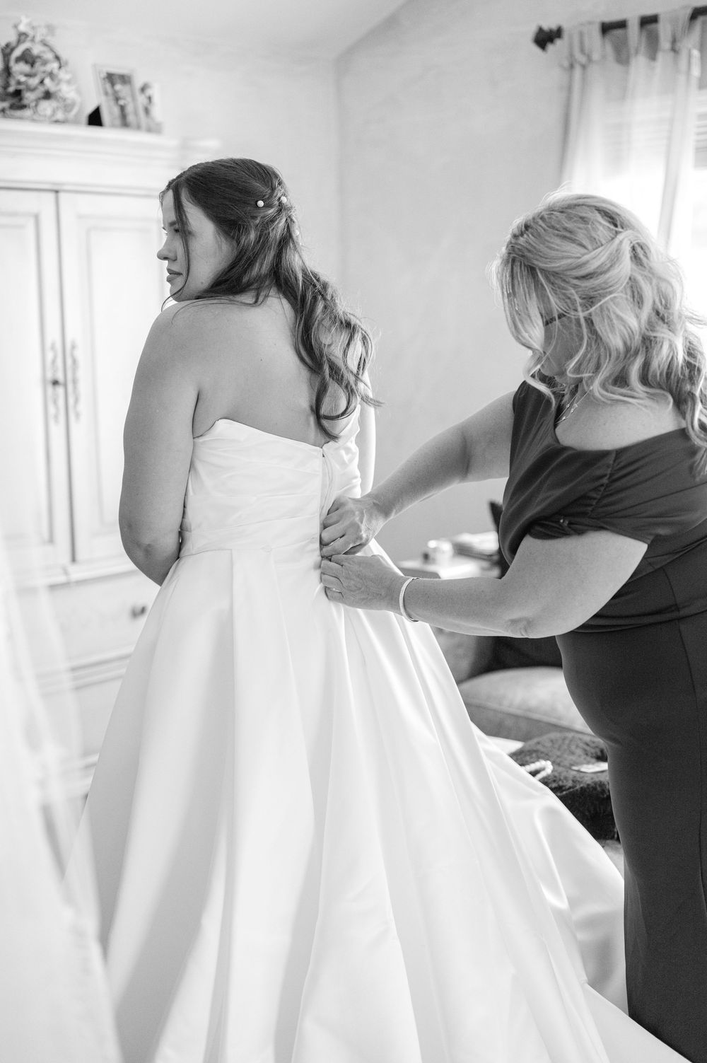 Black and white photo series showing the process of putting on a wedding dress with assistance.