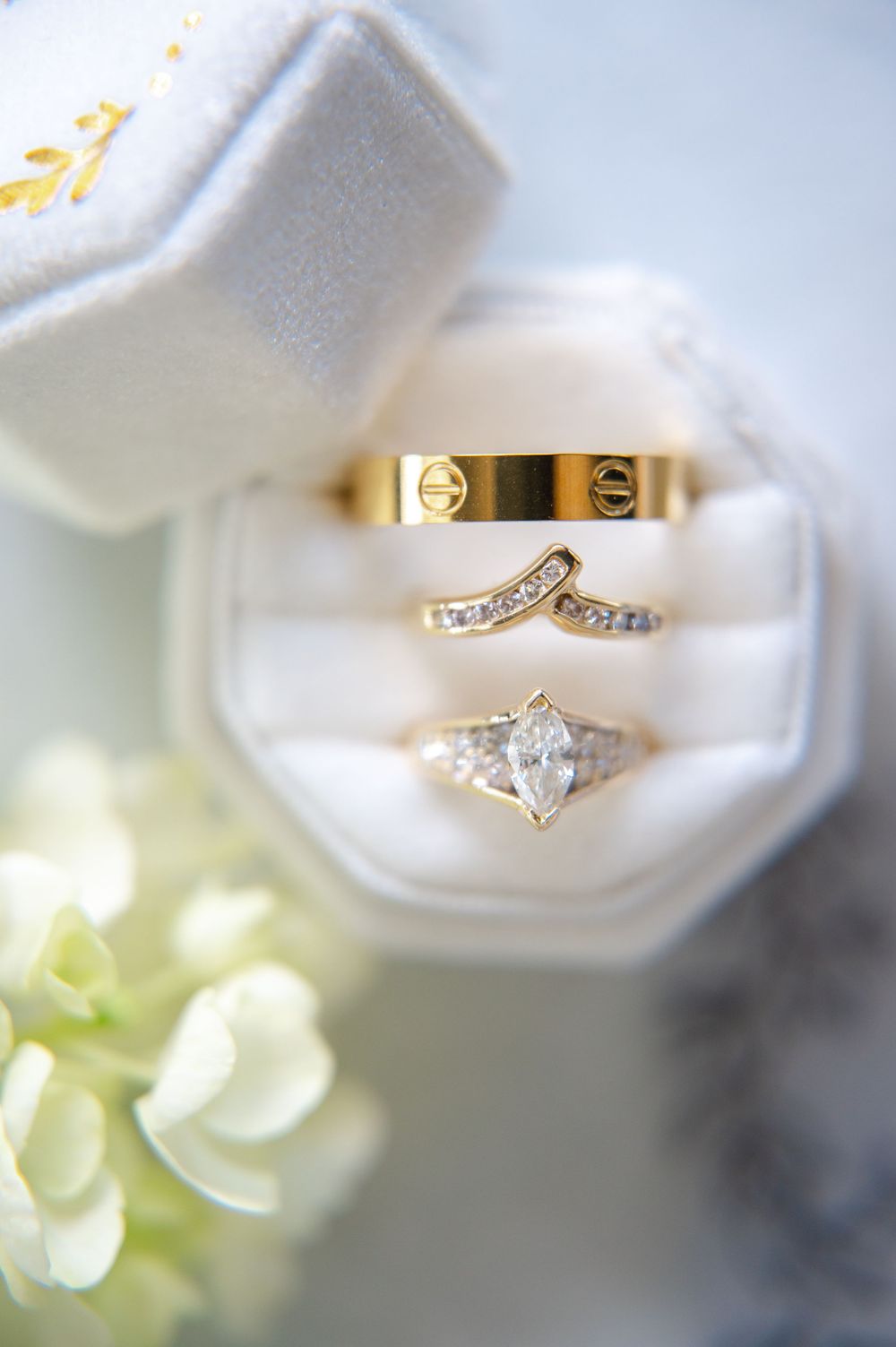 Three elegant wedding rings including a diamond engagement ring displayed in a white ring box with floral decor.