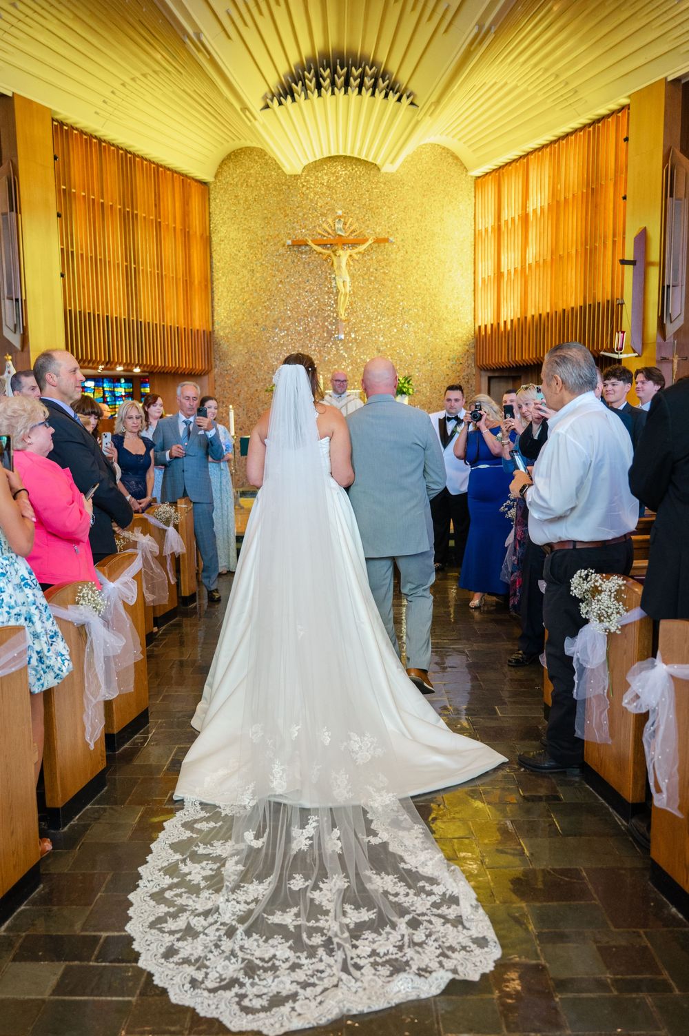 A stunning cathedral wedding ceremony with guests watching as the bride's lace train trails down the aisle.
