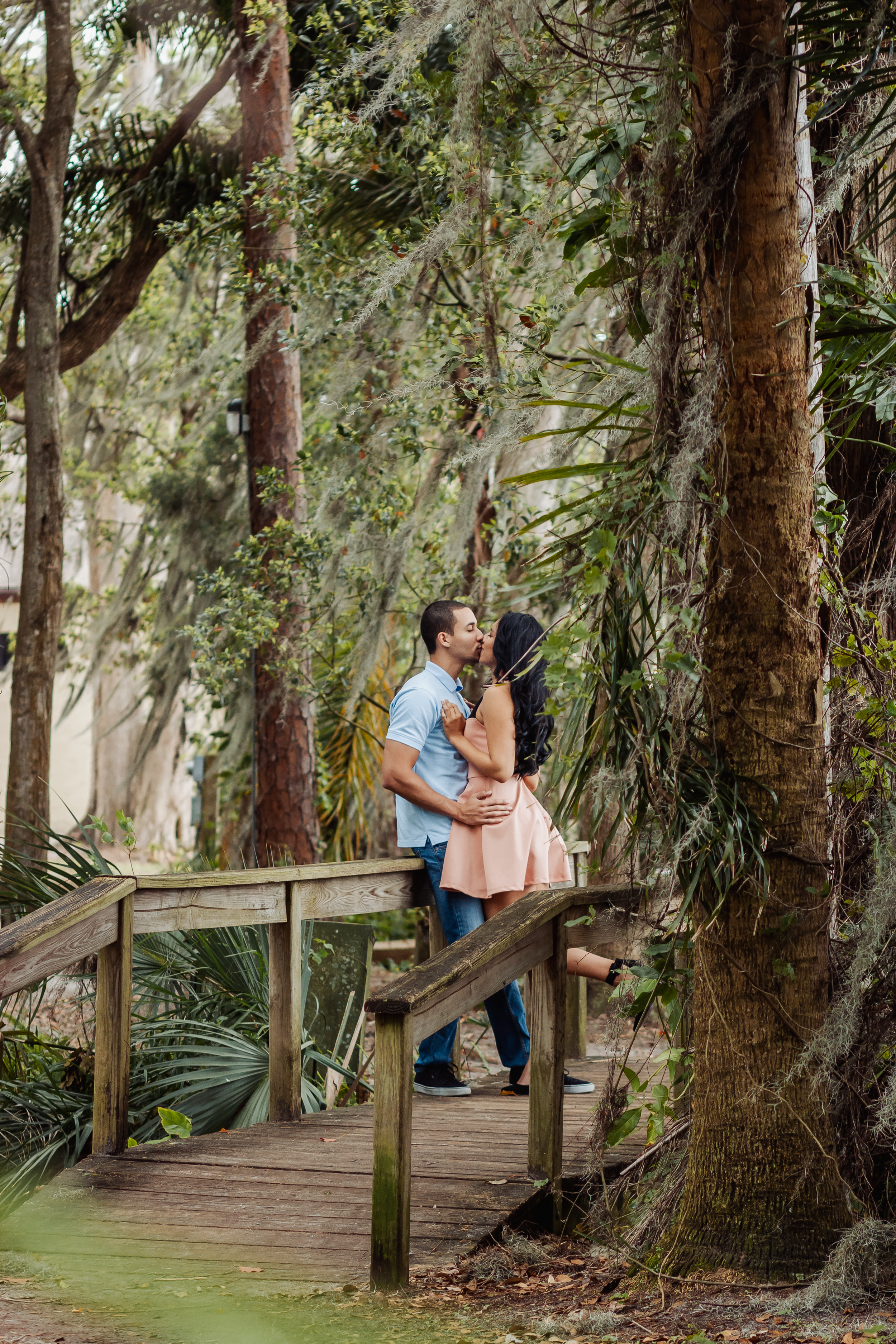 Couple sharing intimate moments on wooden walkway surrounded by Spanish moss trees.