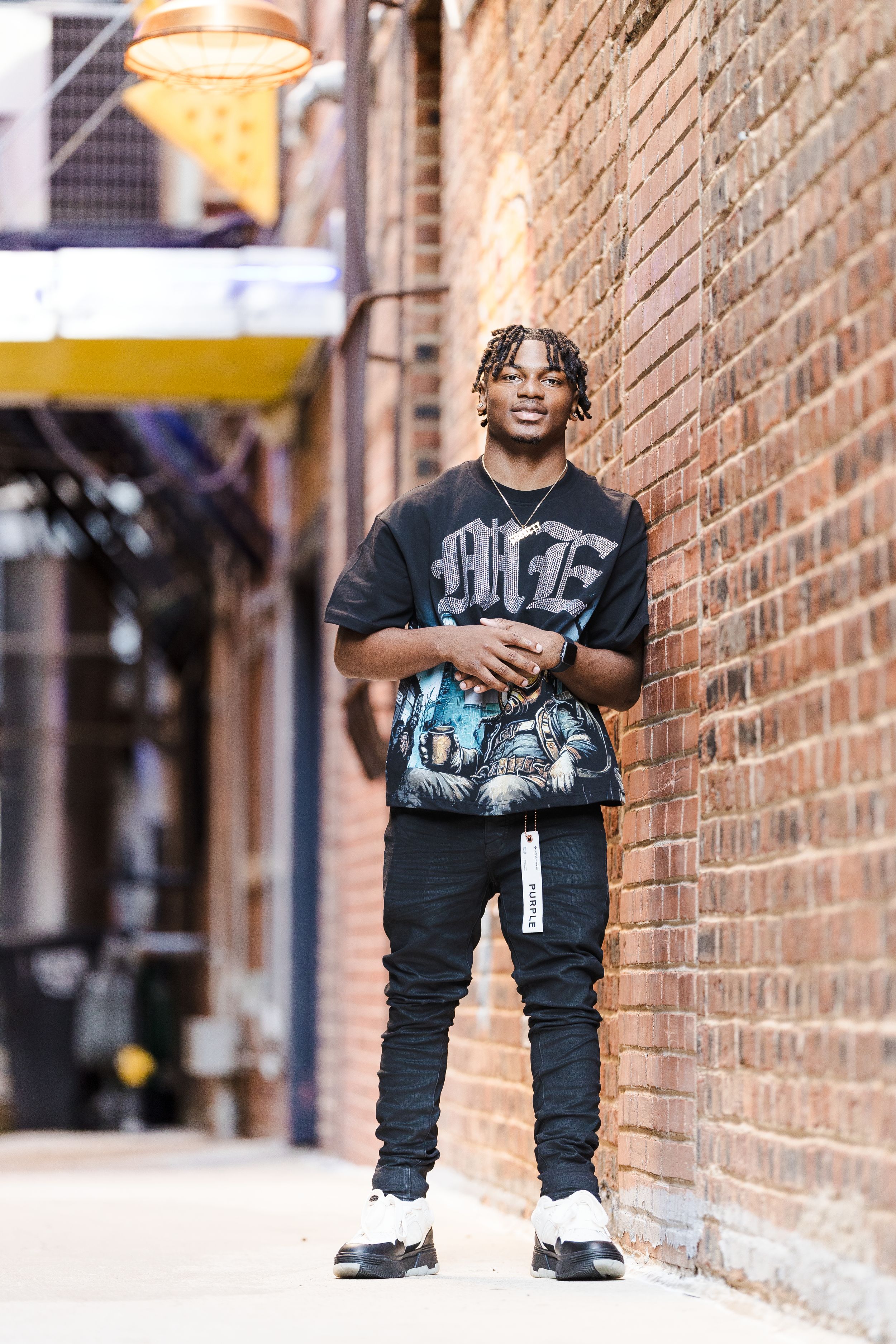 Person wearing casual streetwear posing against brick wall in urban setting.