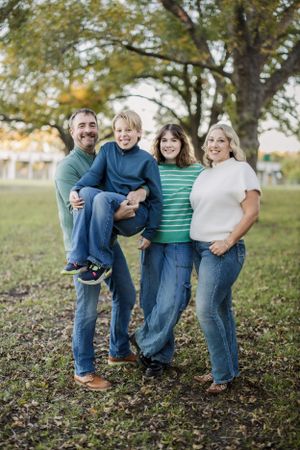 Family wearing coordinated outfits poses together on fallen leaves in a park setting.
