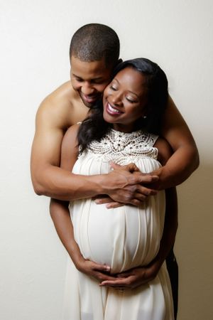 Maternity photo session featuring couple in white against neutral backdrop.