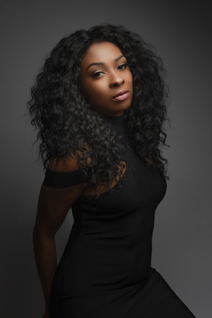 Professional studio portrait with dramatic lighting showcasing elegant black attire and curly hair against dark background.
