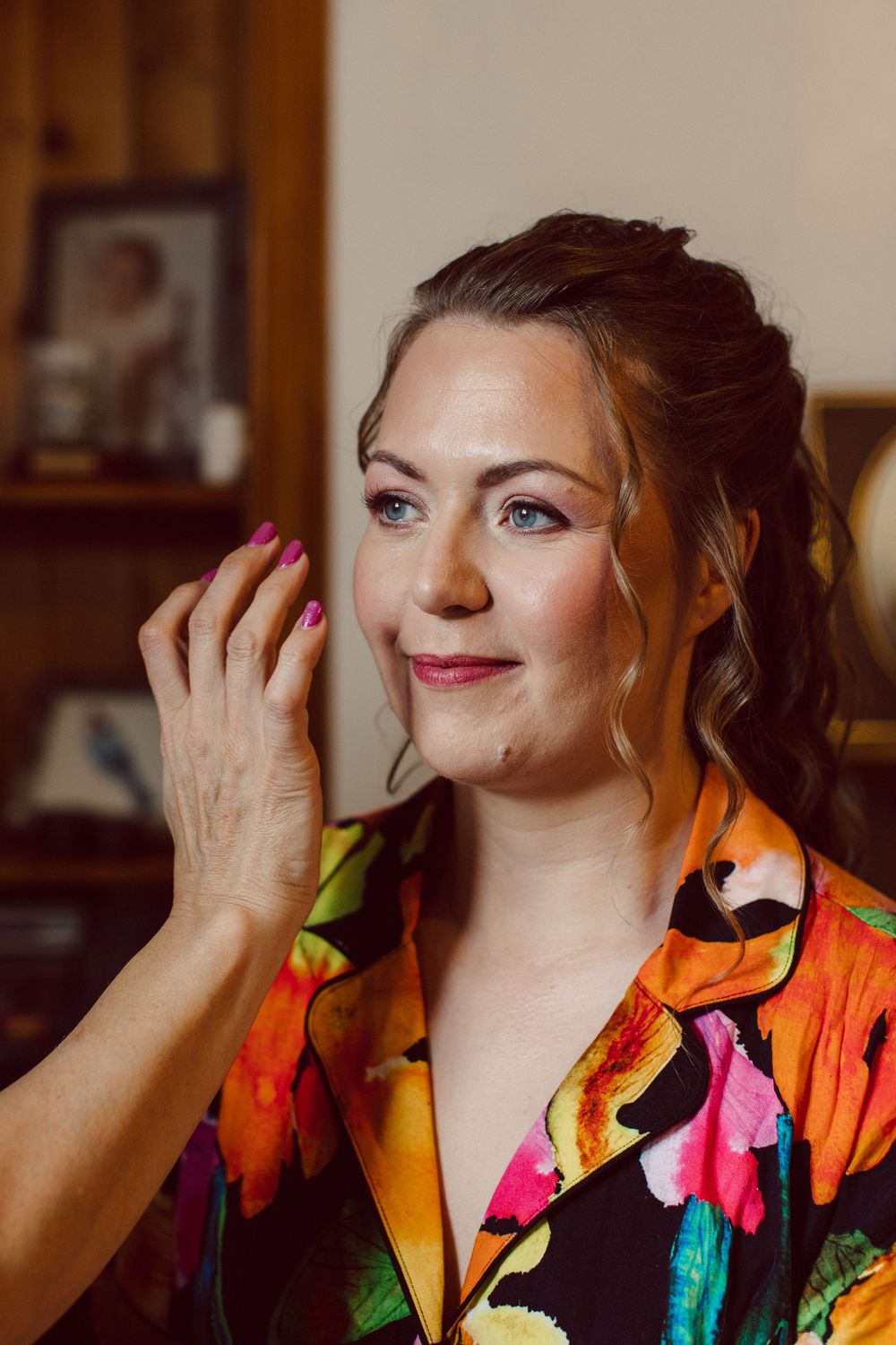 A woman in a vibrant colorful robe touches her face while posing expressively in an indoor setting.