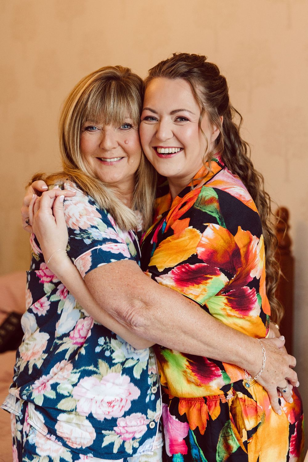 Two women in floral print dresses share joyful hugs and laughter in a series of candid portrait photos.