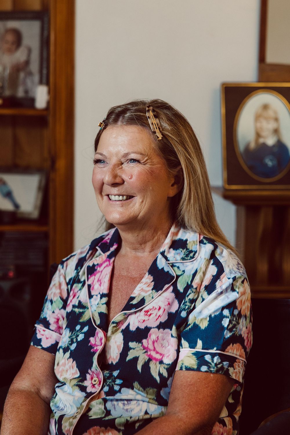 A woman wearing a floral print navy and pink blouse smiles while sitting in a home setting.