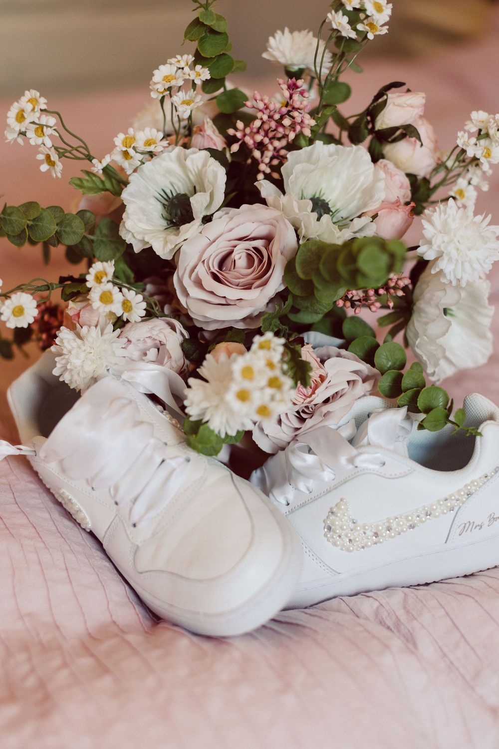 White sneakers filled with delicate flowers including daisies and roses arranged in a romantic wedding styling composition.