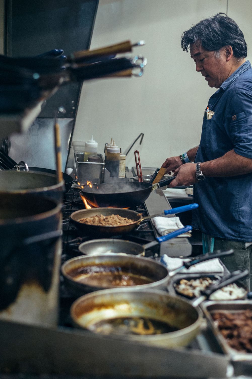 Chef cooking multiple dishes on stovetop in restaurant kitchen.