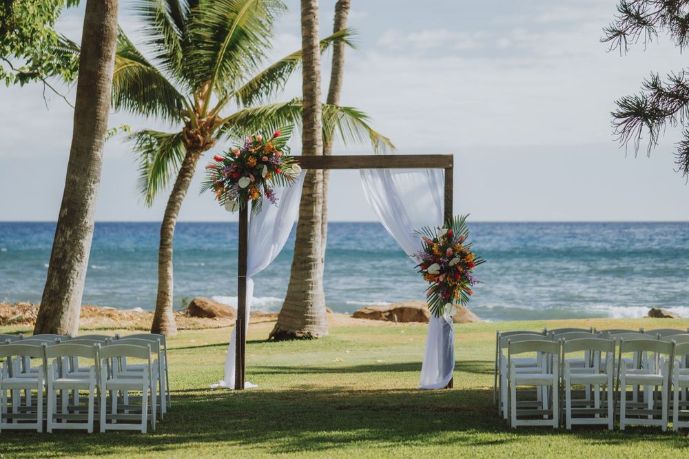 Oceanfront wedding venue with white chairs arranged for ceremony under palm trees.