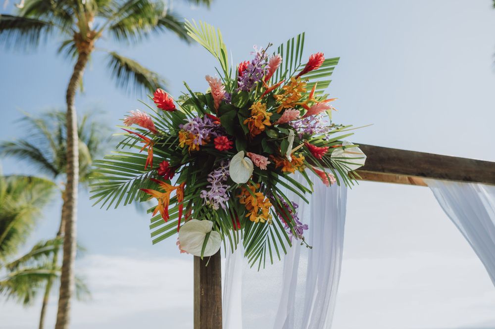 Tropical floral arrangements with bright colors decorate wedding ceremony arch.