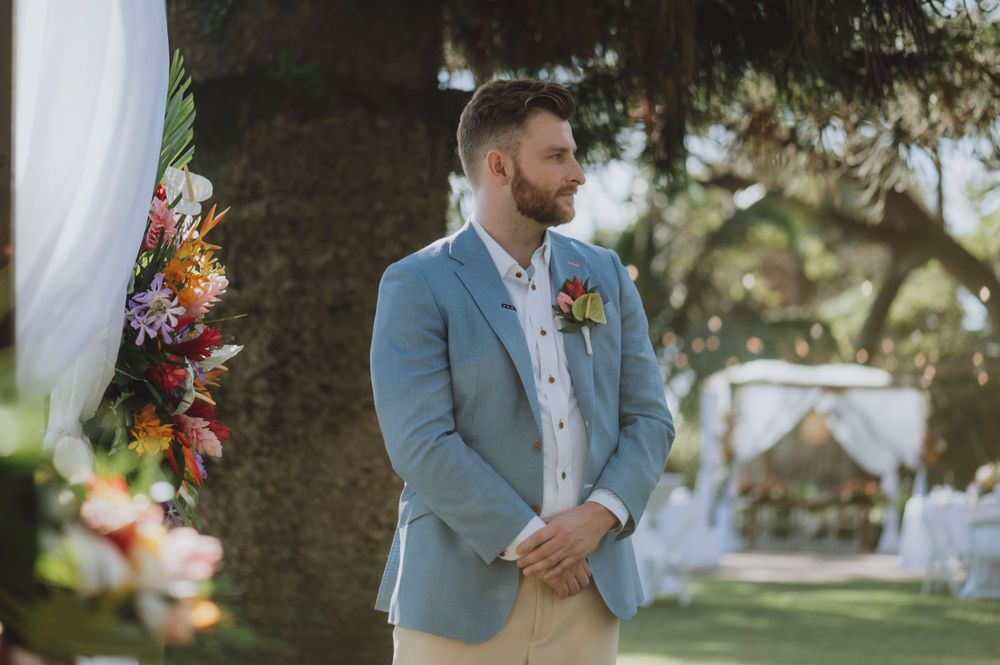 Wedding party members gather outdoors in light blue and white attire for a beach ceremony.