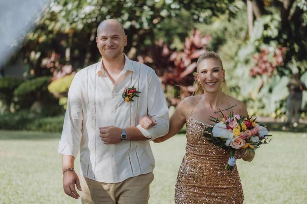 A couple celebrates during a tropical outdoor wedding ceremony with palm trees and ocean views.