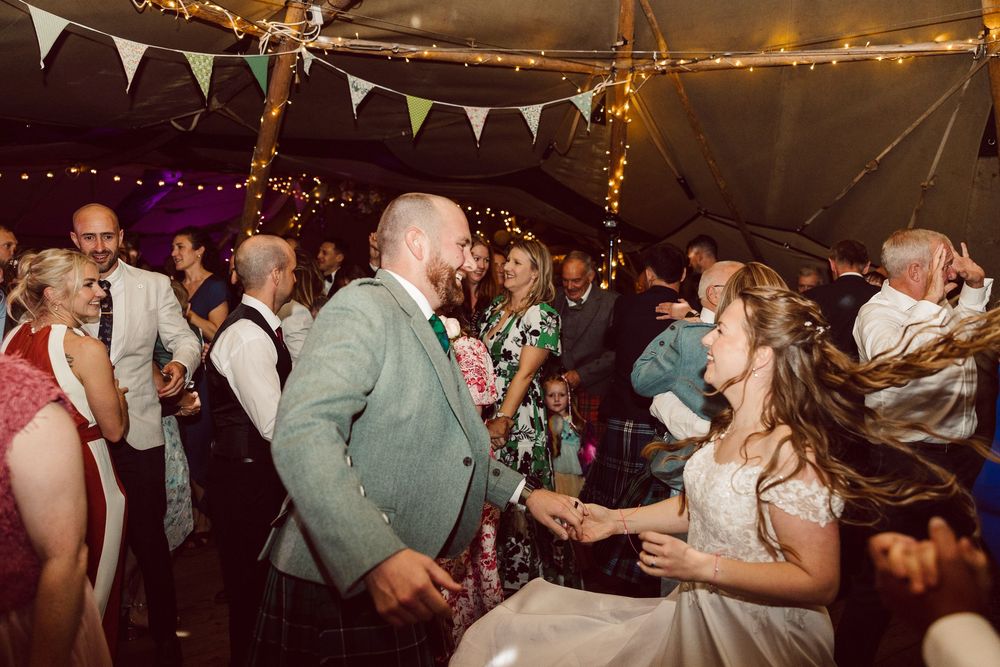 Wedding guests dancing and celebrating on a dimly lit dance floor decorated with string lights and bunting.