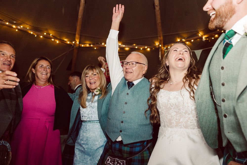 Joyful celebration at a wedding reception with guests dancing under festive string lights.