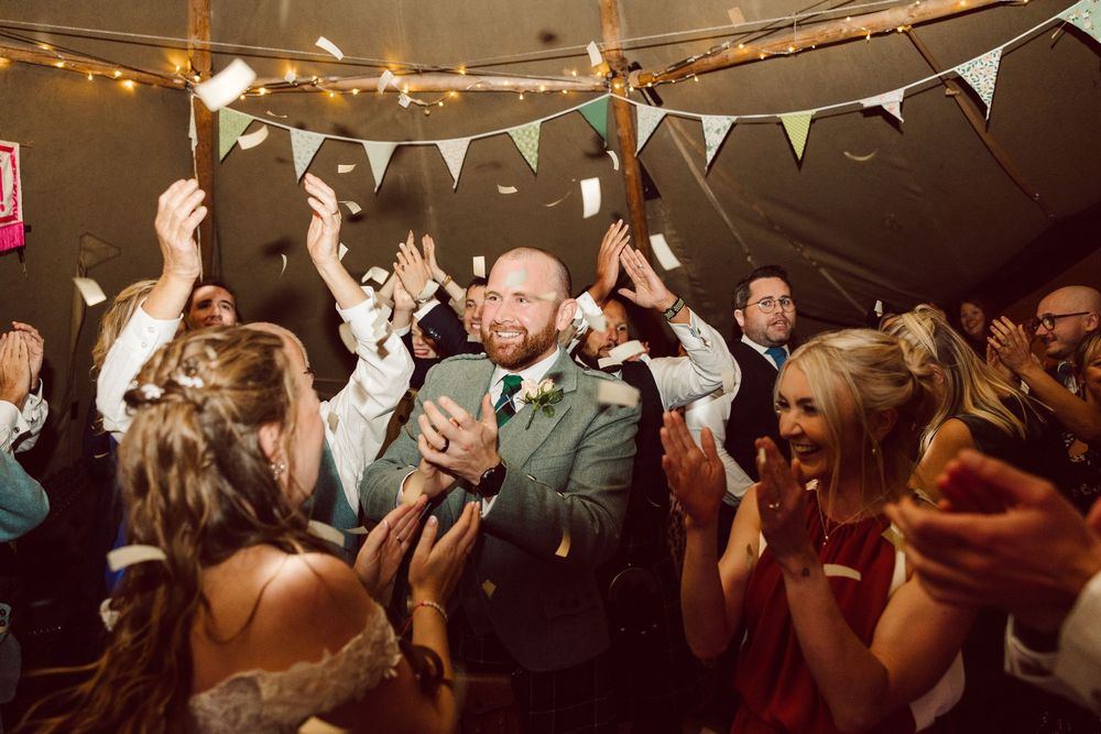 People dancing and celebrating at a lively party with white bunting decorations hanging overhead.