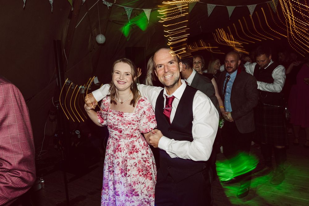 A couple dances together at a festive party with string lights and bunting decorations overhead.