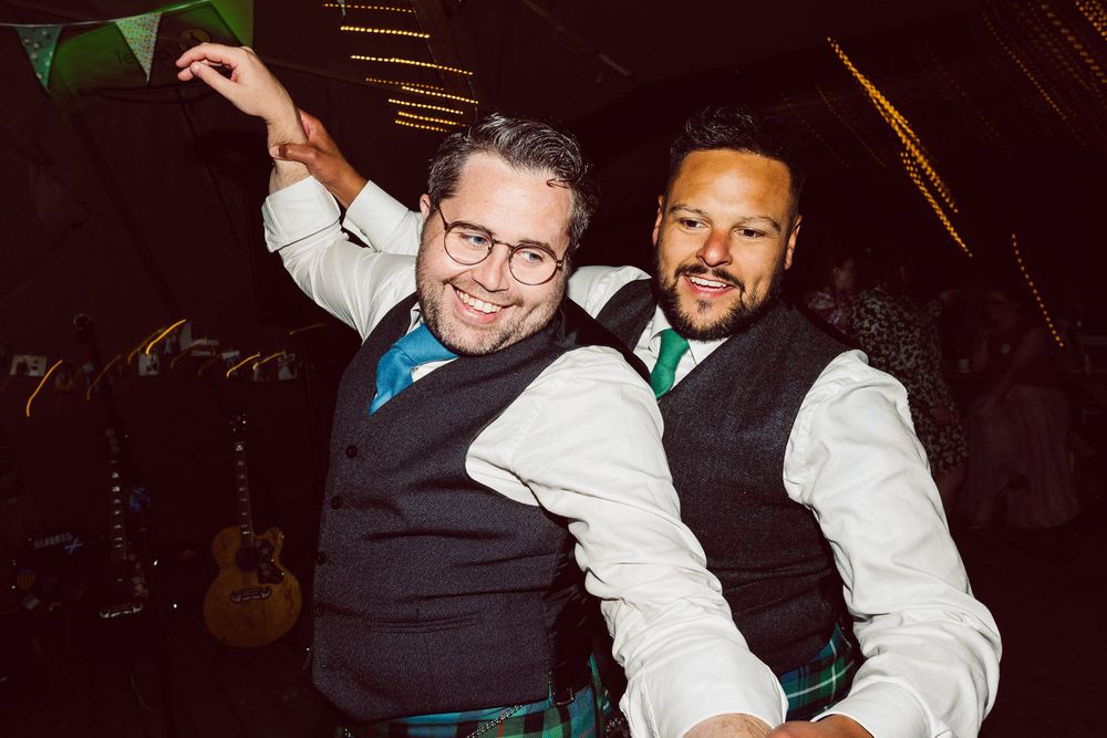 Party guests dancing together under festive green and white bunting at a nighttime celebration.