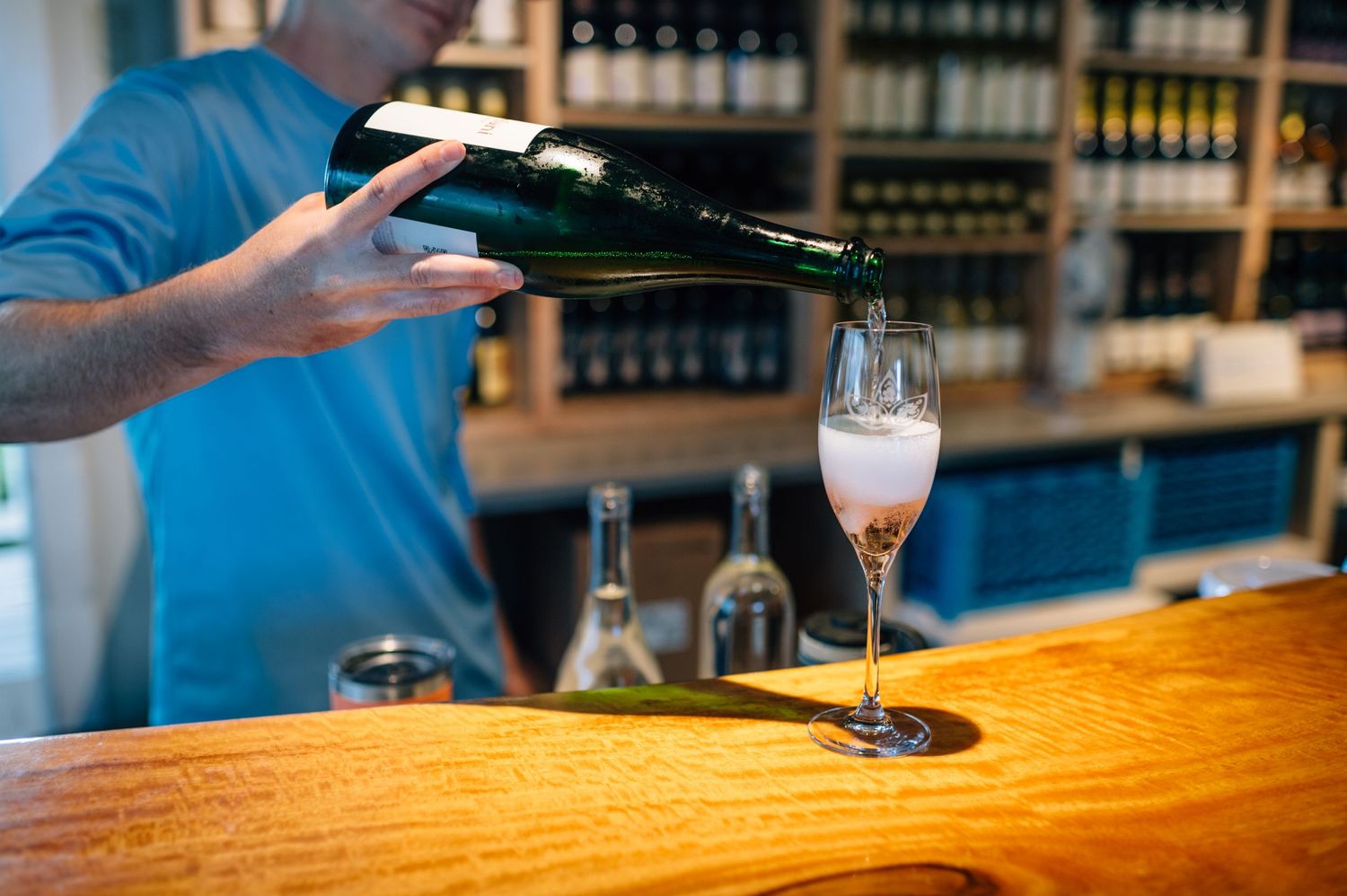 Wine being poured into a glass at a rustic wooden bar counter.