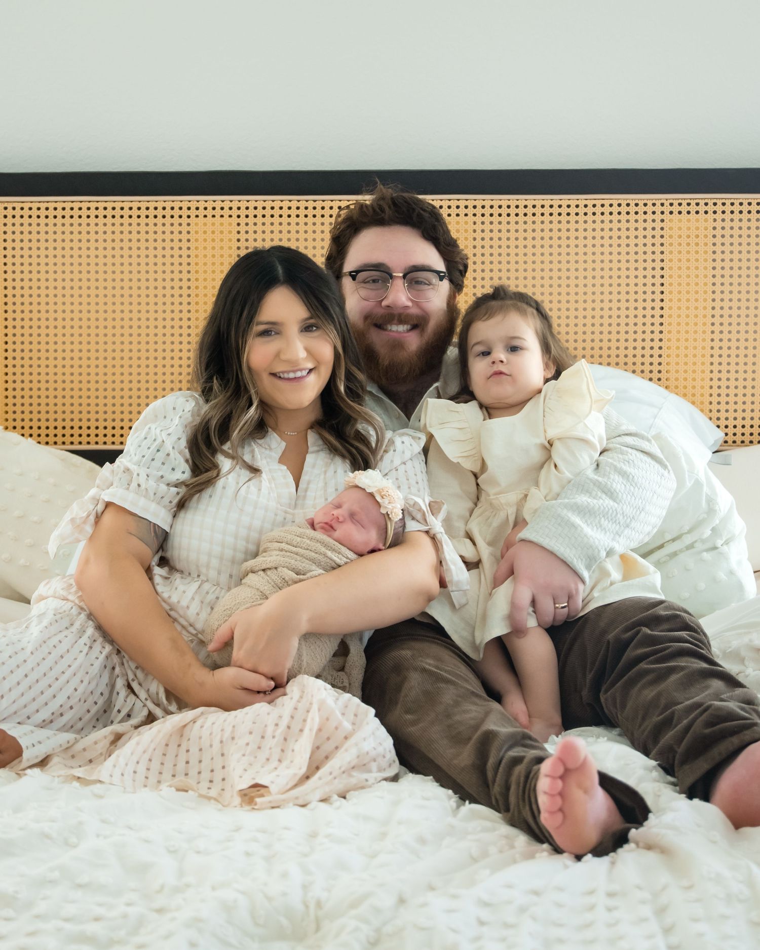 A family lounges together on a white bed wearing casual attire while sharing intimate moments.