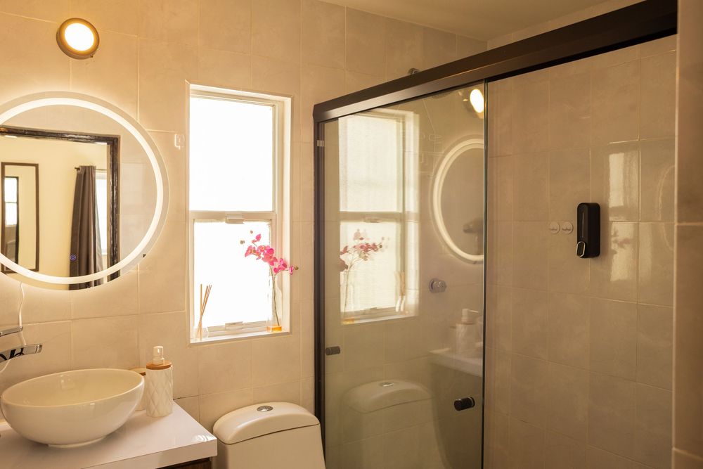 Minimalist bathroom interior with circular mirrors and white walls illuminated by natural light through small windows.
