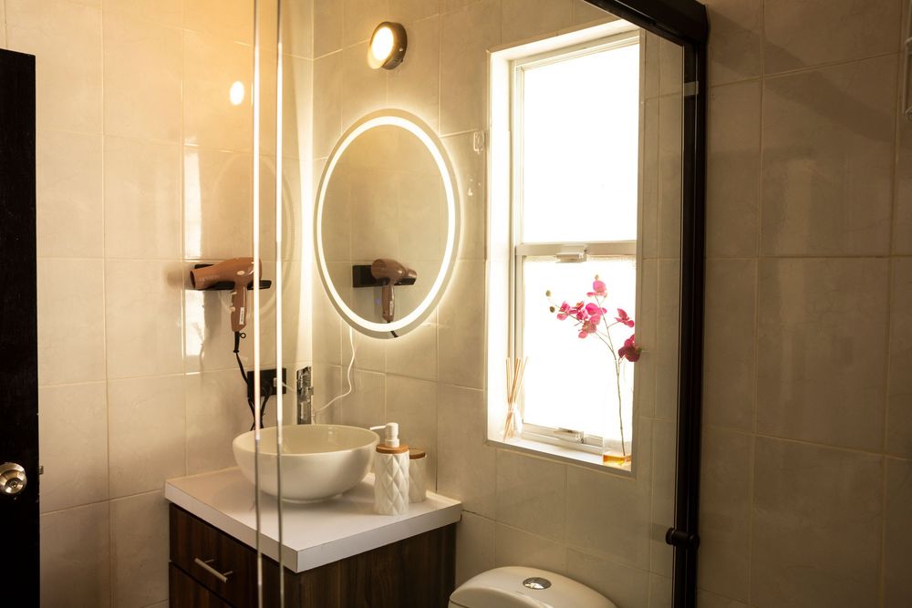 Modern bathroom interior with backlit round mirror, glass shower enclosure, and warm lighting creating an elegant atmosphere.