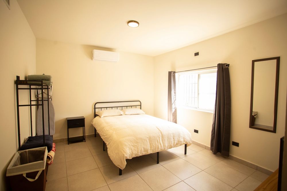 Panoramic view of minimalist bedroom with white bedding and dark curtains.