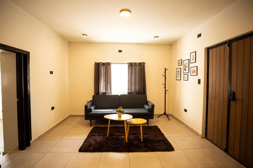 A panoramic view of a modern minimalist bedroom with warm lighting and dark furniture against cream-colored walls.