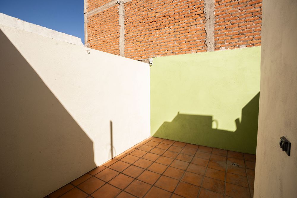 Exterior view of brick wall with terracotta tiles and white painted surfaces under blue sky.