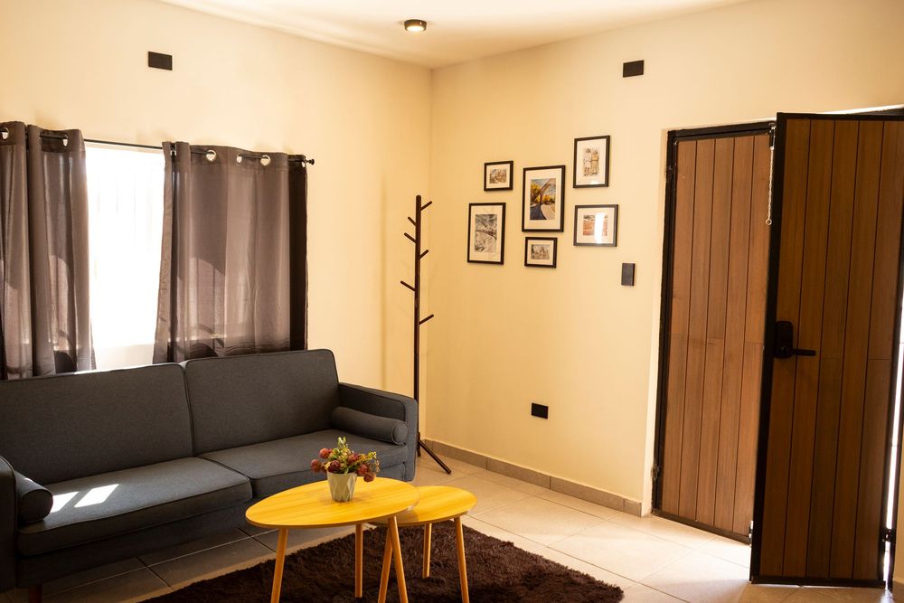 A panoramic view of a modern hotel room interior with beige walls, framed artwork, and dark wood furniture.