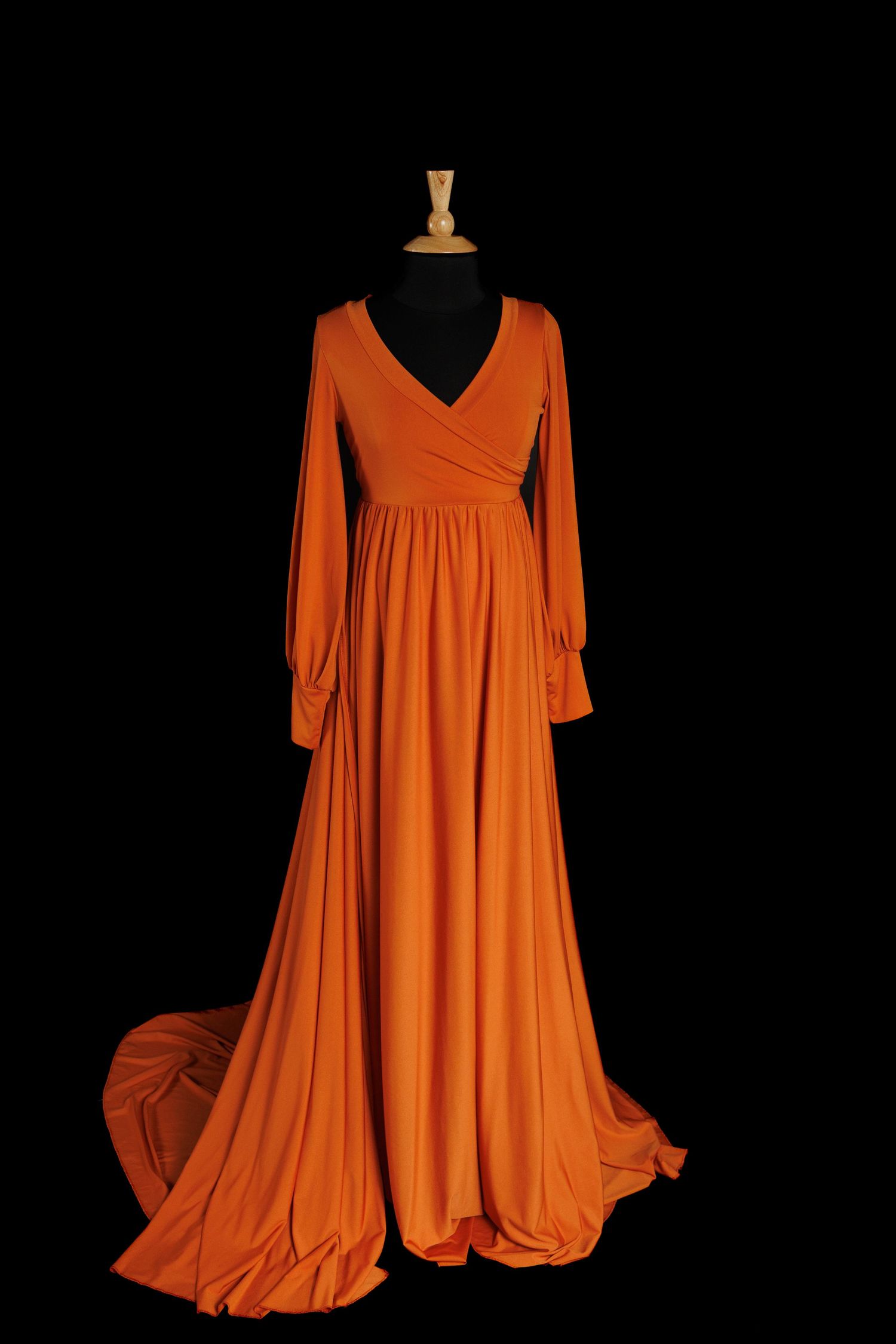 Rust-colored maternity gown with wrap V neckline, long sleeves, empire waist, and flowing floor-length skirt.