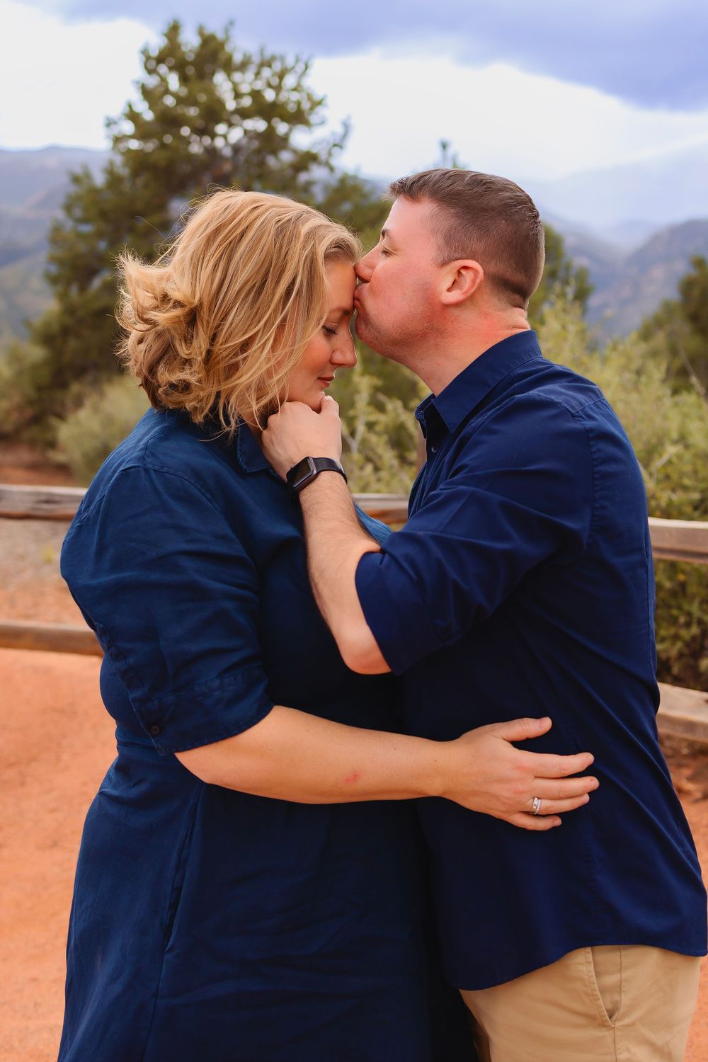 A couple in matching navy tops share an intimate moment outdoors against a mountain backdrop.