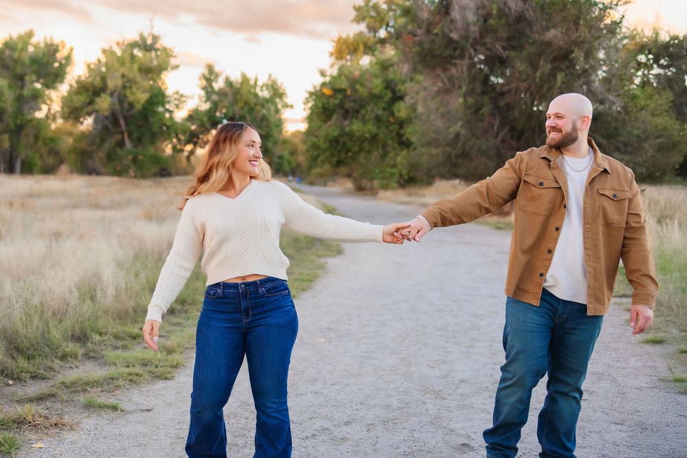 Couple in casual attire walking hand in hand on a gravel path during sunset.