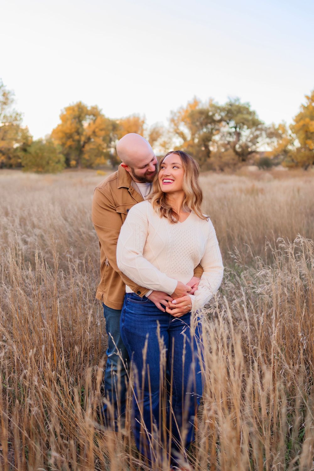 A couple shares joyful moments together while standing in a golden autumn field during sunset.