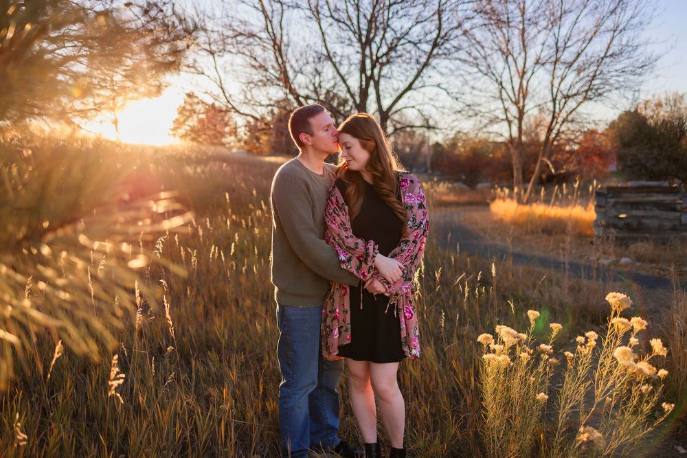 A couple embraces in a golden sunlit field during sunset, surrounded by tall grass and warm autumn colors.