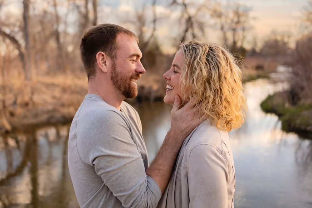 Romantic couple embraces by a tranquil lake during golden hour in a scenic autumn landscape.
