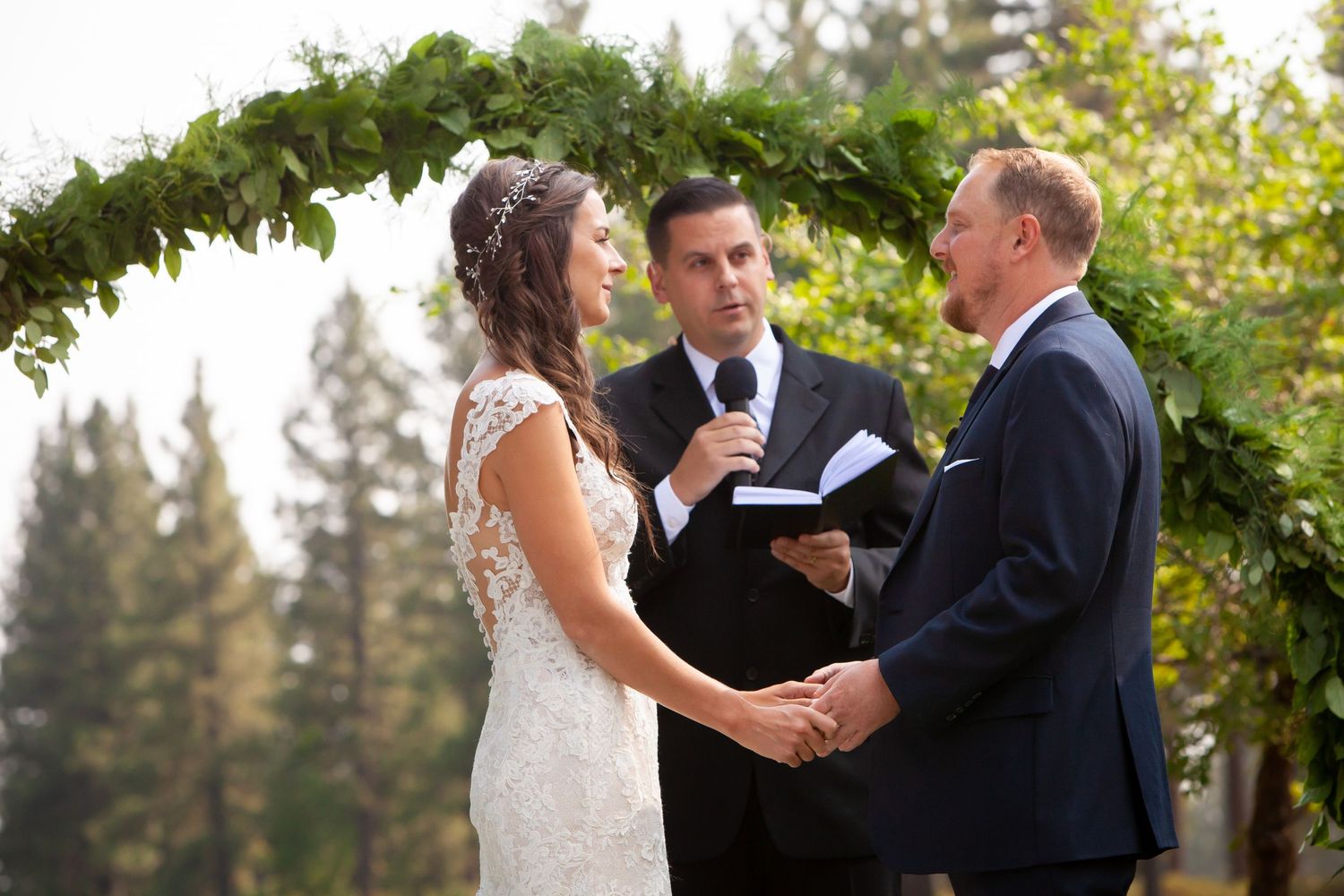 A romantic wedding couple shares a kiss in a lush green garden setting while holding a white bouquet.