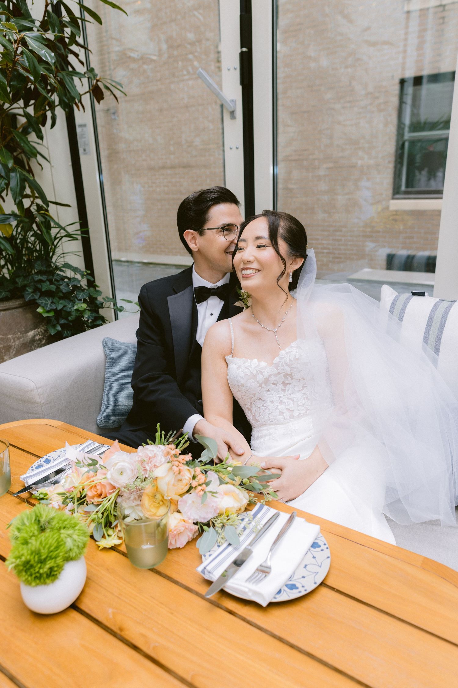 A couple shares a romantic moment at a wooden table decorated with floral arrangements and place settings.