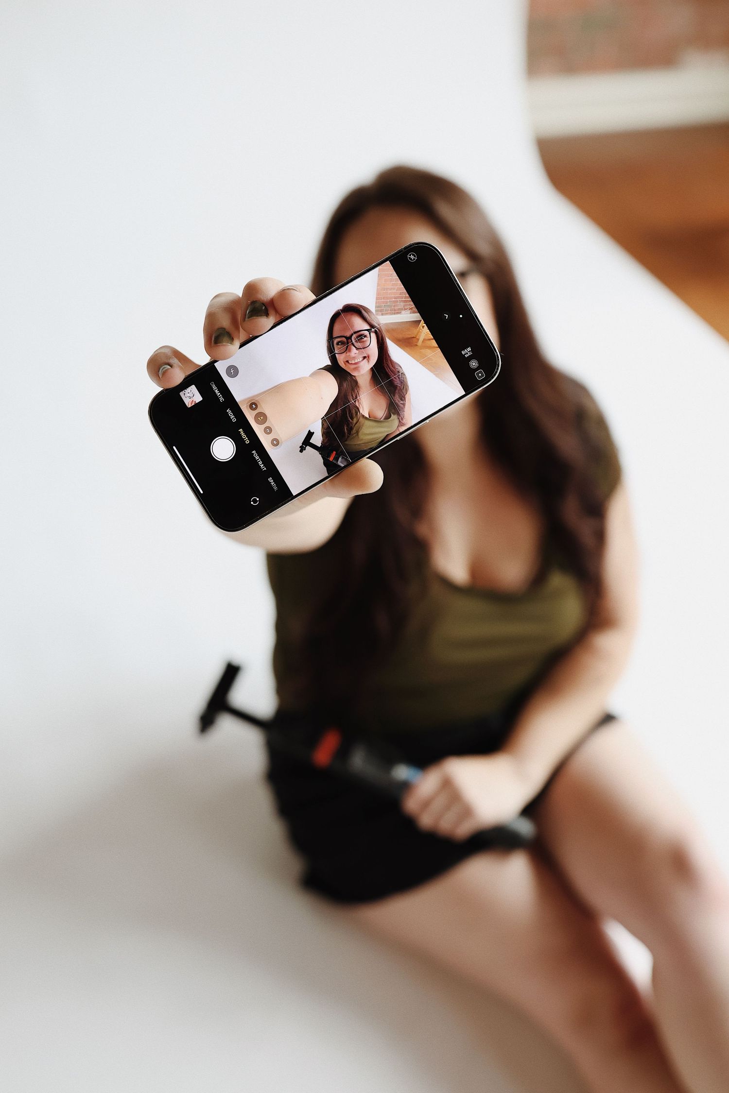 Person taking a selfie with a smartphone while sitting, showing the phone screen displaying the photo being taken.